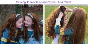 Two girls in dress up clothes for little girls. Each girl wears My Hair Popz brown princess hair which is secured to a rhinestone tiara. One girl is brushing the curly princess hair her friend is wearing. One girl wears her brown princess hair straight.